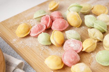 Wooden board with colorful raw dumplings and flour on white background, closeupの写真素材