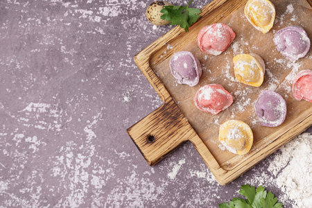 Wooden board with colorful raw dumplings and flour on dark backgroundの写真素材