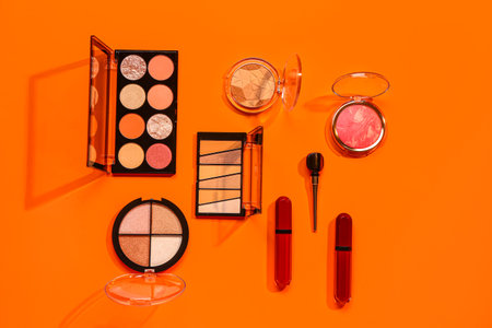 Beautiful palettes of eyeshadows and different decorative cosmetics on orange backgroundの写真素材