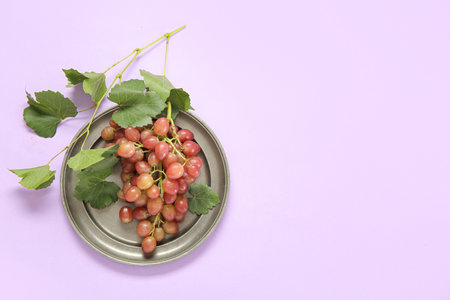 Plate with tasty ripe grapes on lilac backgroundの写真素材