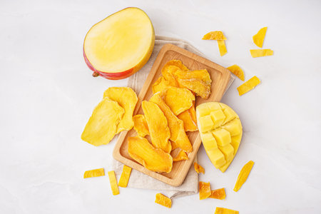 Wooden board with slices of dried mango on white backgroundの写真素材