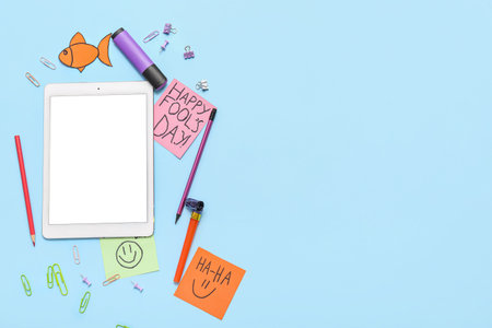 Modern tablet, paper clips and sticky notes on blue background. April Fools Day prank