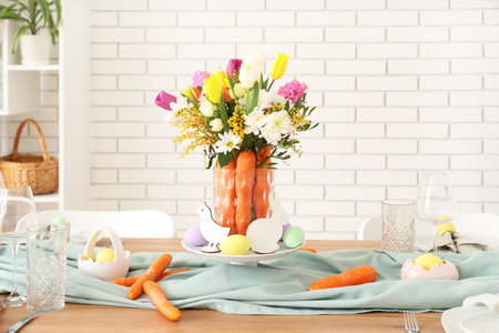 Beautiful table setting for Easter decorated with bouquet of carrots and flowers near white brick...