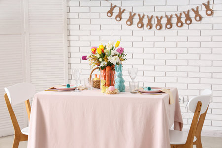 Beautiful table setting for Easter decorated with bouquet of carrots and flowers near white brick...