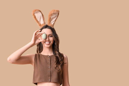 Happy young woman in bunny ears headband with Easter egg on beige background