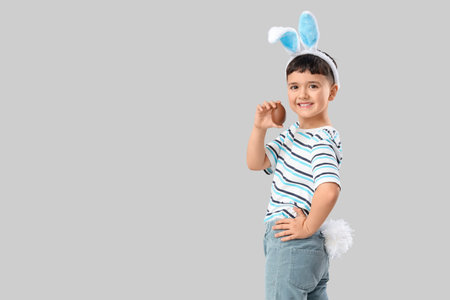 Cute little boy in bunny ears headband with chocolate egg for Easter on white background