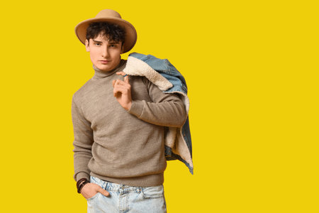 Handsome young man in stylish clothes and hat on yellow backgroundの写真素材
