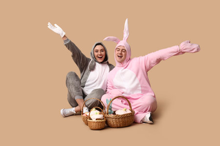 Beautiful young couple in bunny costume with Easter baskets sitting against brown background