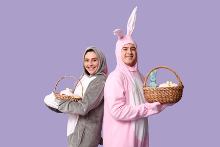 Beautiful young couple in bunny costume with Easter baskets on purple background