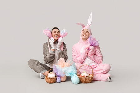 Beautiful young couple in bunny costume with Easter baskets and gift eggs sitting on gray background