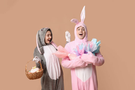 Beautiful young couple in bunny costume with Easter basket and gift eggs on brown background
