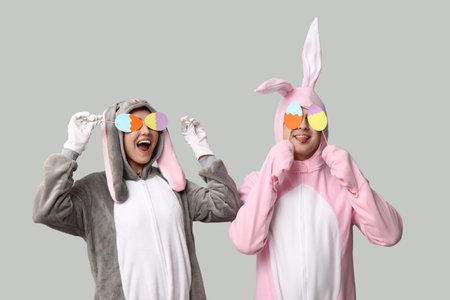 Beautiful young couple in bunny costume with paper Easter eggs on gray background