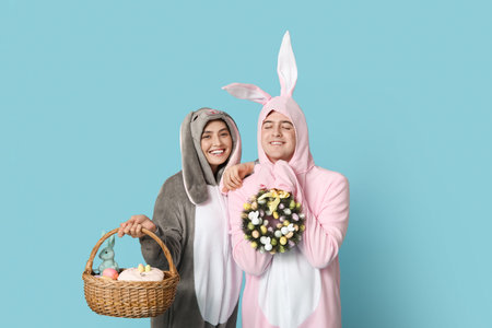 Beautiful young couple in bunny costume with Easter basket and wreath on blue background