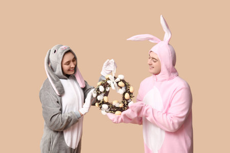 Beautiful young couple in bunny costume with Easter wreath on brown background