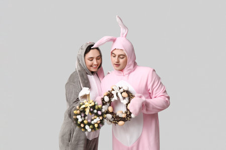Beautiful young couple in bunny costume with Easter wreaths on gray background