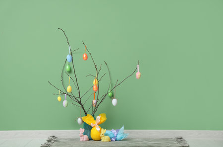 Branches decorated with Easter eggs in vase near color wall