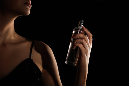 Pretty woman with bottle of perfume on black background