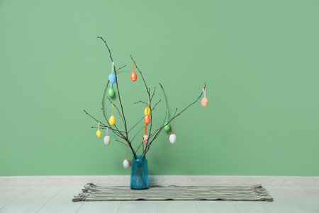 Branches decorated with Easter eggs in vase near color wall