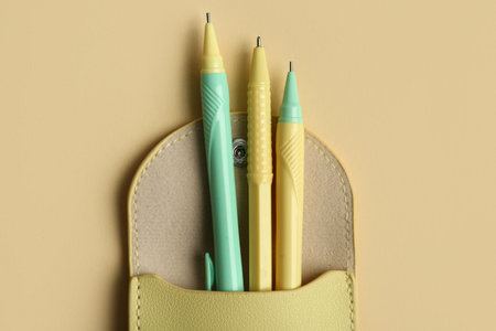 Three pens in pencil case on beige background. Top view