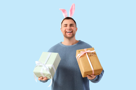 Happy young man in bunny ears with gift boxes on blue background. Easter celebration