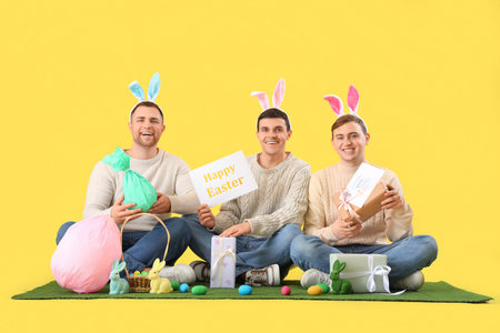 Happy young men in bunny ears celebrating Easter on yellow backgroundの写真素材
