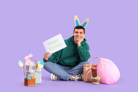 Happy young man in bunny ears celebrating Easter on purple background