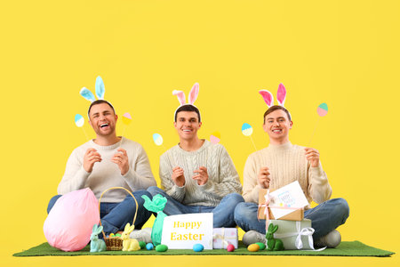 Happy young men in bunny ears celebrating Easter on yellow background