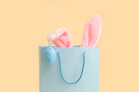 Shopping bag with fluffy bunny ears and Easter egg on beige background