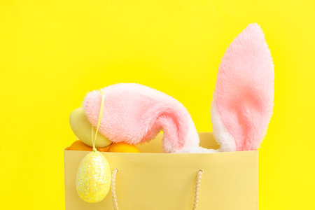 Shopping bag with fluffy bunny ears and Easter eggs on yellow background