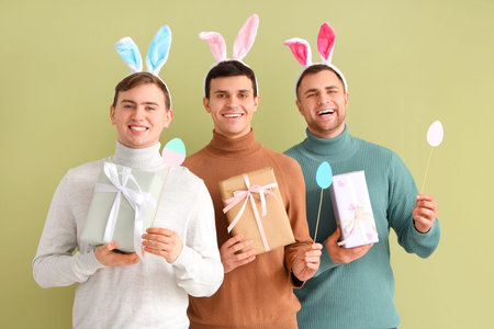 Happy young men in bunny ears with gift boxes and paper eggs on green background. Easter celebrationの写真素材