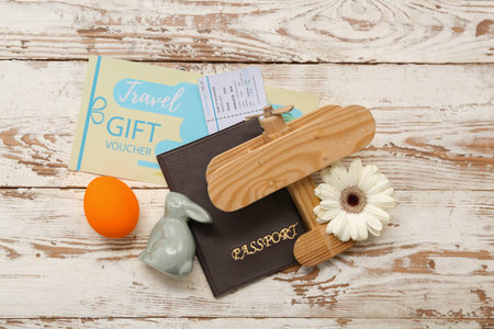 Toy plane with passport, ticket and Easter decor on light wooden background. Holiday travel...