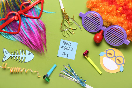 Colorful wigs with funny glasses, party whistles and sticky notes on green background. April Fools Dayの写真素材