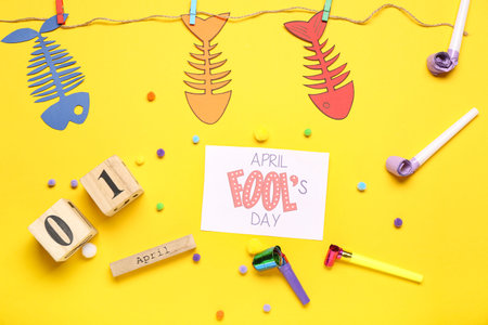 April Fool's Day card with calendar, paper fishes and party whistles on yellow backgroundの写真素材
