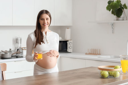 Young pregnant woman with glass of juice in kitchenの写真素材