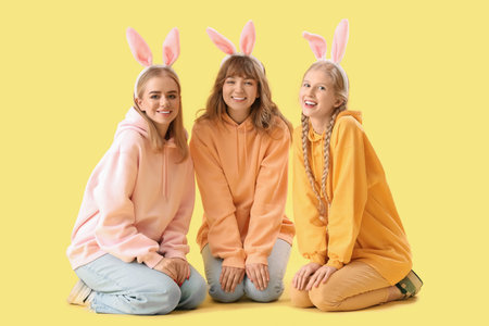 Young girls with Easter bunny ears on yellow background