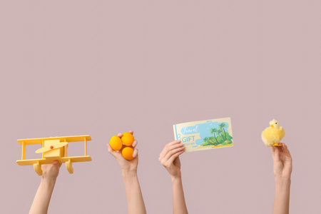 Female hands holding gift vouchers with toy plane, chicken and Easter eggs on pink background....