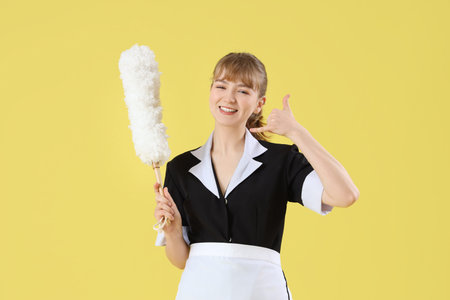 Young chambermaid with pp-duster showing call me gesture on yellow background