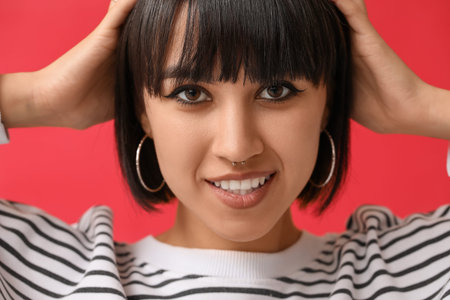 Stylish young woman with nose piercing on red background, closeup