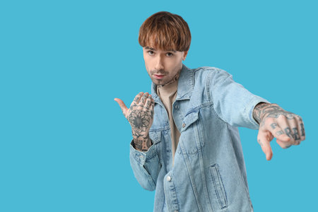 Young tattooed man dancing against blue background