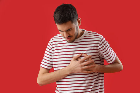 Young man suffering from chest pain on red background