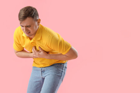Young man suffering from chest pain on pink background