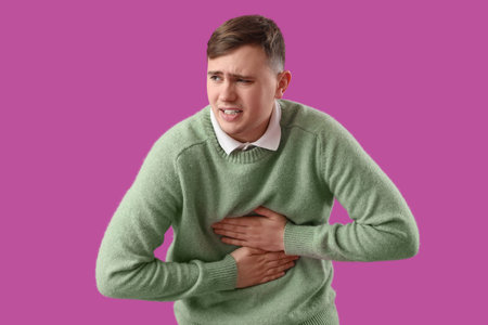 Young man suffering from chest pain on purple background