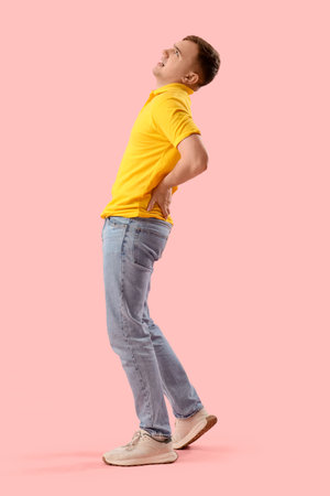 Young man suffering from back pain on pink backgroundの写真素材