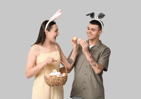 Happy young couple with Easter basket and bunny ears on gray background