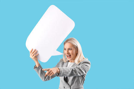 Angry mature woman with blank speech bubble pointing at something on blue background. Accusation...