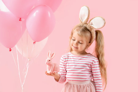 Cute little girl in bunny ears with toy rabbit and balloons on pink background. Easter celebrationの写真素材