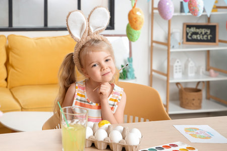 Thoughtful little girl in bunny ears painting Easter eggs at home