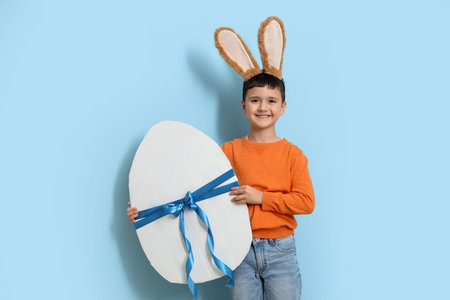 Cute little boy with bunny ears and big Easter egg on blue background
