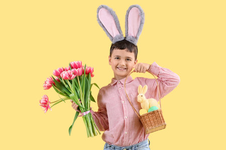 Cute little boy with bunny ears, Easter eggs and tulip flowers and on yellow background