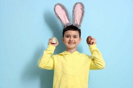 Cute little boy in bunny ears with chocolate Easter eggs on blue background